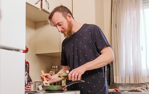 blond man with beard wearing dark blue shirt is cooking at the stove